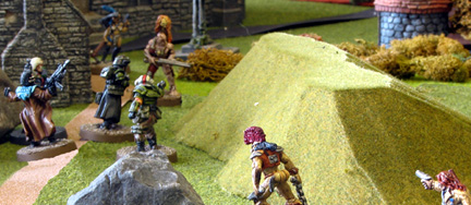 Rather than becoming stalled in a fire fight, the Mercs race up the path to the village and eventual safety, ignoring the Savages who are thus able to get round the rear of the Mercs. It’s not looking good!

As the Mercs gain the edge of the village, terrifying Berserkers appear in front of them as well as more Savages. The Mercs deal with a Savage directly ahead of them and storm into the village. In the far distance can be seen the door to the refuge that is their objective.